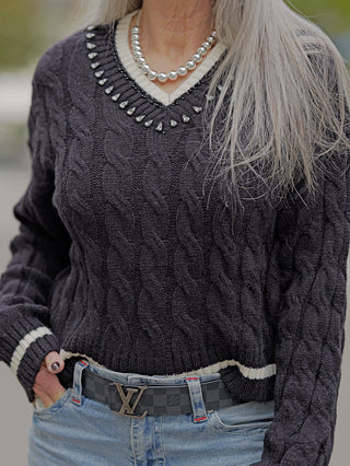 Eine Frau trägt den OFF#DLY Pulli Berta in Schwarz, ein kurzer, schmaler Zopfmuster-Pulli mit V-Ausschnitt und Strasssteinen, ergänzt durch eine modische Halskette.