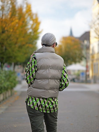 Person trägt die OFF#DLY West Ronja taupe, eine kurze Steppweste mit Stehkragen und seitlichen Taschen, während sie auf der Straße geht.