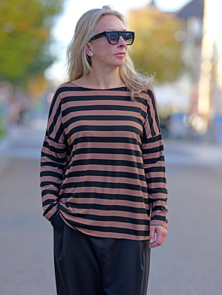 Frau trägt das OFF#DLY Ringel Grosso black/caramel, ein gestreiftes Shirt mit Rundhals und geschnittenen Kanten. Sie kombiniert es mit Sonnenbrille für einen modischen Look.