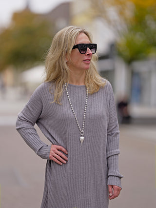 Frau trägt das OFF#DLY Dress Clara grey, ein gerades Strickkleid mit Rundhals, kombiniert mit Sonnenbrille und grauem Pullover. Perfekt für legere Mode und Streetstyle.