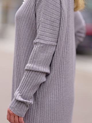 Person trägt das OFF#DLY Dress Clara grey, ein gerades Strickkleid mit Rundhals und langen Ärmeln. Das Design betont die schlichte Eleganz des Kleids, ideal für kühle Tage.