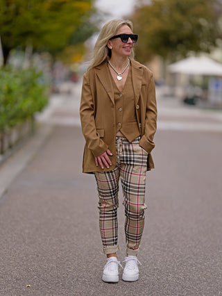 OFF#DLY Blazer Gianna camel in Oversized-Passform, getragen von einer Frau auf dem Gehweg, kombiniert mit karierter Hose und weißen Sneakers. Enthält seitliche Taschen und Knopfleiste.
