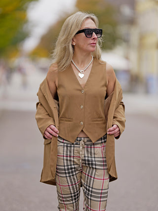 OFF#DLY Weste Julia camel getragen von einer Frau mit Sonnenbrille, zeigt seitliche Taschen und Knopfleiste. Sie trägt eine Kette und eine Jacke, passend für Street-Fashion-Looks.