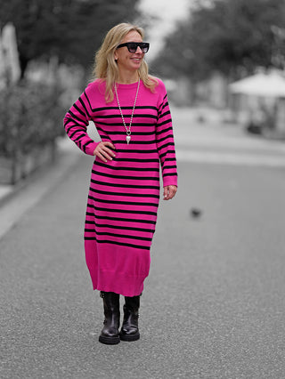Frau trägt das OFF#DLY Ringelkleid pink mit schwarzen Streifen, Rundhalsausschnitt, ohne Taschen. Das Kleid ist knielang und wird mit Sonnenbrille kombiniert, ideal für modische Straßenauftritte.