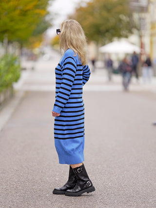 Frau trägt das OFF#DLY Ringelkleid blue mit blauen und schwarzen Streifen, kombiniert mit schwarzen Stiefeln. Das Kleid hat einen Rundhalsausschnitt und besteht aus Viskose und Nylon.
