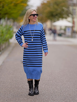 Frau trägt das OFF#DLY Ringelkleid blue, ein knielanges, blau-schwarz gestreiftes Kleid mit Rundhals. Kombiniert mit schwarzen Stiefeln und Sonnenbrille für einen schicken Street-Fashion-Look.