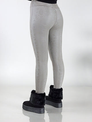 Person trägt OFF#DLY Snake Legging taupe mit schwarzen Stiefeln. Nahaufnahme von schwarzem Stiefel mit grauem Stoff und Fellbesatz. Leggings aus 95% Polyester, 5% Elastan.