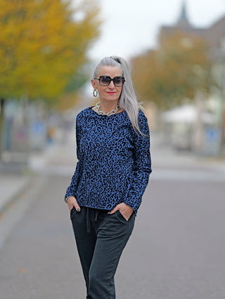 Frau trägt OFF#DLY Shirt Cindy blue mit Rundhals und Allover-Leo-Flockprint, kombiniert mit Sonnenbrille und schwarzer Hose.