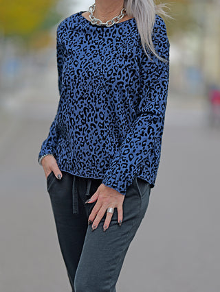 OFF#DLY Shirt Cindy blue, getragen von einer Frau, zeigt ein blau-schwarzes Leopardenmuster, Rundhalsausschnitt und lange Ärmel. Der Fokus liegt auf dem einzigartigen Leo-Flockprint.