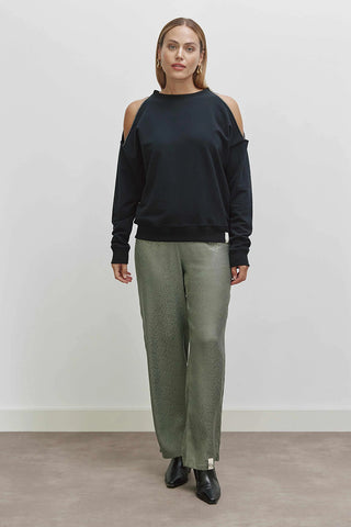 Frau trägt das Cotton Candy Lisbeth Sweat mit Rundhalsausschnitt und Metallic-Naht an der Schulter. Kombiniert mit grüner Hose und schwarzen Stiefeln für einen lässigen Look.