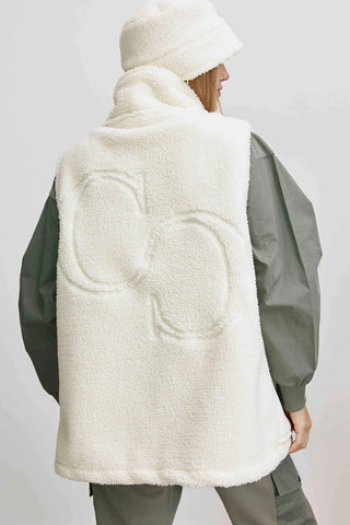 Person von hinten in einer oversized Cotton Candy Lina Weste aus cremefarbenem Teddyfleece mit hohem Kragen und doppeltem C-Logo, kombiniert mit passendem flauschigen Hut und olivefarbenem Langarm-Outfit darunter.
