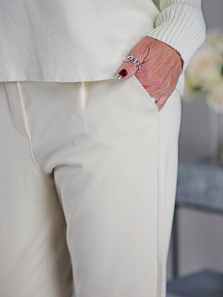Nahaufnahme von OFF#DLY Joggpant Doris beige mit einer Hand in der Seitentasche. Die Hose zeigt Bundfalte, Gummibund und Kordelzug, getragen von einer Person.