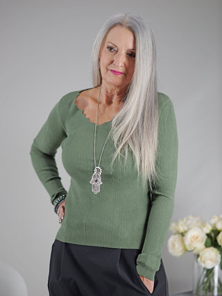 OFF#DLY Longsleeve Nina khaki, getragen von einer Frau mit langen grauen Haaren, zeigt einen V-Ausschnitt und eine gerade Passform, kombiniert mit einem modischen Halsketten-Accessoire.