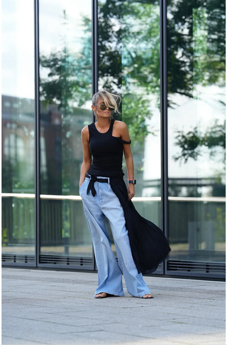 Frau trägt das Gitta Banko Monique Top schwarz mit Cut-Out-Design, kombiniert mit blauer Jeans. Das eng anliegende Ripptop hebt sich durch sein modisches Detail ab.