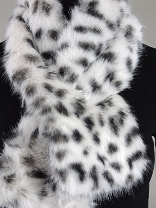 Der OFF#DLY Fake Fur Schal Sandra leo zeigt ein weiches, weißes Kunstfell mit unregelmäßigen schwarz-grauen Flecken im Schneeleopardenmuster, drapiert über einem schwarzen Hintergrund.