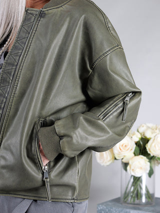 Person trägt die OFF#DLY Fake Lederjacke Sina khaki im Pilotenstil mit Strickbund und Zippern, hält ein Glasvase mit weißen Rosen.