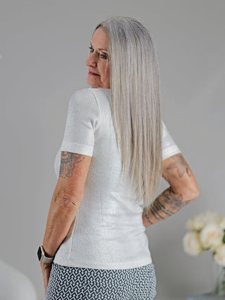Frau mit tätowiertem Arm trägt das stilvolle OFF#DLY Top Sindy weiß/silber, ein eng anliegendes Feinripp-Top mit silbernem Lurex-Faden und Rundhalsausschnitt.