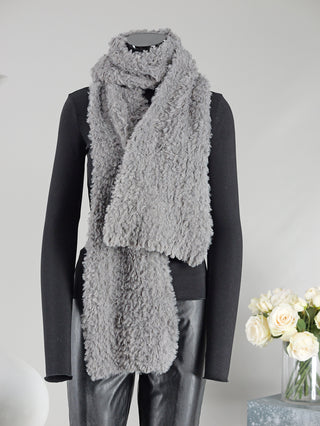 Mannequin mit OFF#DLY Schal Lola grau, ein langer Fakefurschal aus 100% Polyester, Größe 200x20 cm, neben einem Blumenstrauß in einer Glasvase.