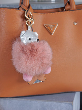 Nahaufnahme des OFF#DLY Bag Charm Bär silber/rose, einem Taschenanhänger aus Kunstfell, mit silbernen Details. Sichtbar ist das Design des Bären auf einem braunen Lederuntergrund. Größe ca. 10x10 cm.