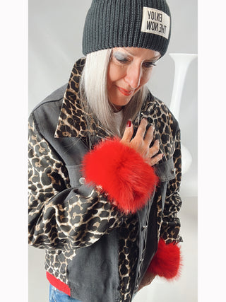 Eine Frau trägt den OFF#DLY Pulswärmer rot aus Kunstfell mit Gummizug, kombiniert mit einem Leopardenmantel und Beanie.