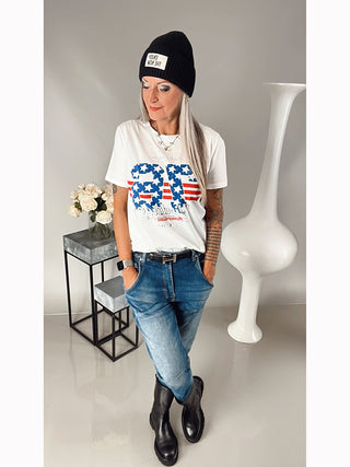 Frau trägt das OFF#DLY Tee Vintage weiß mit blau/rot/silbernem Print im US-Style und geradem Schnitt, kombiniert mit Jeans.