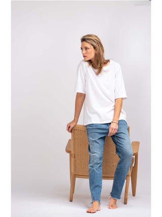 Frau sitzt auf Stuhl, trägt das True Religion Boxy Crew Tee in Weiß, lockerer Schnitt, kombiniert mit Jeans, betont lässigen Stil.