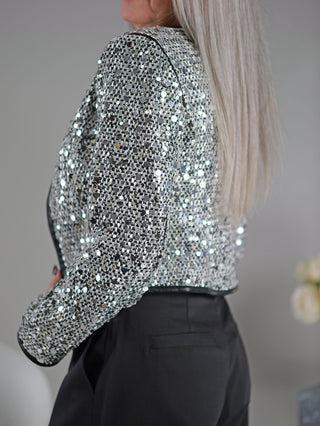 Eine Frau trägt die OFF#DLY Jacke Mila silber/black, eine kurz geschnittene glänzende Jacke mit Zipper und Pailettenbesatz.