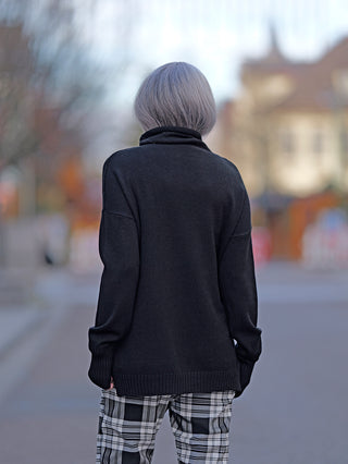 Person auf dem Bürgersteig trägt den OFF#DLY Rolli Clara schwarz, einen schwarzen Rollkragenpullover mit plaid Hose. Der Rolli hat eine normale, gerade Passform und besteht aus Nylon, Viskose und Polyester.