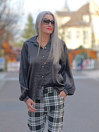 Frau mit grauem Haar, Sonnenbrille und rotem Lippenstift trägt die OFF#DLY Bluse Jutta schwarz mit weiten Ärmeln und Knopfleiste, leicht oversized geschnitten.