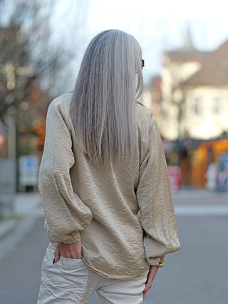 Frau mit langen grauen Haaren trägt die OFF#DLY Bluse Jutta beige mit weiten Ärmeln und Knopfleiste, leicht oversized geschnitten, in einer urbanen Umgebung.