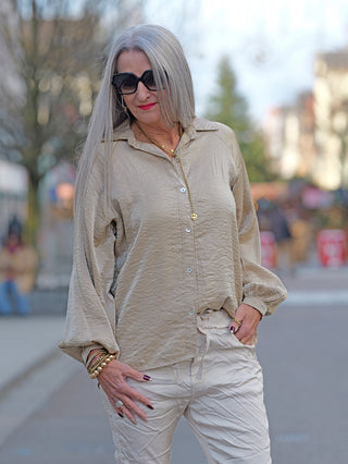 OFF#DLY Bluse Jutta beige: Frau mit grauem Haar trägt beige Bluse mit weiten Ärmeln, Knopfleiste, goldener Kette, und Sonnenbrille. Bluse leicht oversized, hinten länger geschnitten.