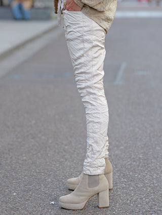 OFF#DLY Pant Olga champagner zeigt schmale Joggpants mit Brokat-Einsatz und Gummibund. Sichtbar sind weiße Stiefel, die das modische Ensemble ergänzen.