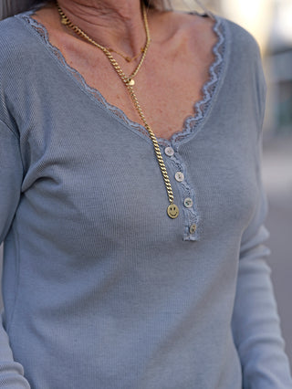 Frau trägt die OFF#DLY LS Maribel grau, ein Feinripp-Longsleeve mit V-Ausschnitt und Spitzenbesatz, sichtbare Knopfleiste am Hals, passend von Größe 34 bis 42.