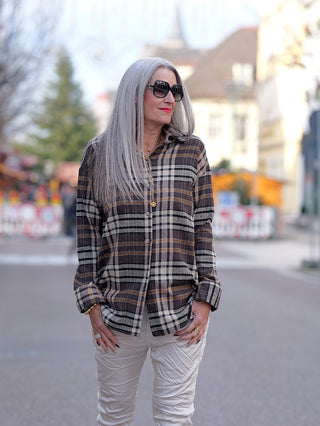 Frau trägt die OFF#DLY Bluse Karo mit Knopfleiste und Karomuster. Gerade Passform, sichtbar mit weißen Hosen und Sonnenbrille. Ideal für Street Fashion, aus Baumwolle, Polyester, Viskose.