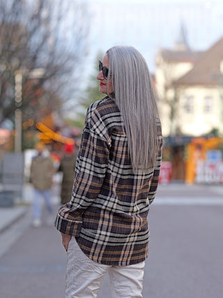 Frau mit Sonnenbrille trägt die OFF#DLY Bluse Karo, eine Hemdbluse mit Knopfleiste und Karomuster, während sie draußen steht, modisch in einem urbanen Umfeld.