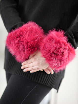Person in schwarzer Kleidung trägt OFF#DLY Pulswärmer pink aus Kunstfell an beiden Handgelenken, die mit einem Gummizug versehen sind.