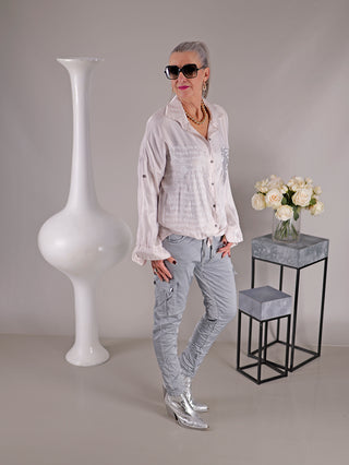Frau trägt OFF#DLY Bluse Ulrike rosa mit Print und Pailletten auf der Brusttasche, steht neben einer Vase mit weißen Rosen.