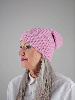 Frau trägt OFF#DLY Mütze Anna rosa, eine pinke Strickmütze im Beanie-Stil. Deutlich sichtbare, hochwertige Verarbeitung mit markanten Strickdetails, passend für modische Akzente im Alltag.