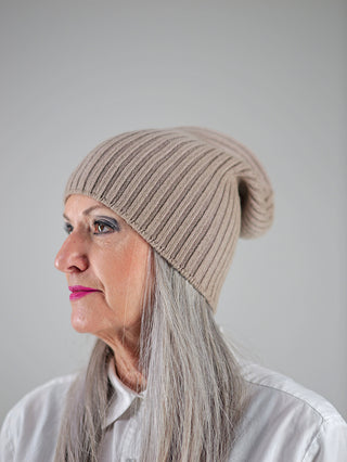 Eine Frau trägt die OFF#DLY Mütze Anna taupe, ein stilvolles Strickaccessoire perfekt für kalte Tage, mit einer weichen Textur, die bequem auf dem Kopf sitzt.
