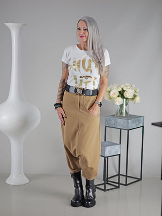 Frau trägt das OFF#DLY Tee Shut up, mit Print Shut up. Sie steht vor einer Vase mit weißen Rosen. Das T-Shirt hat kurze Ärmel und eine schmale Passform.