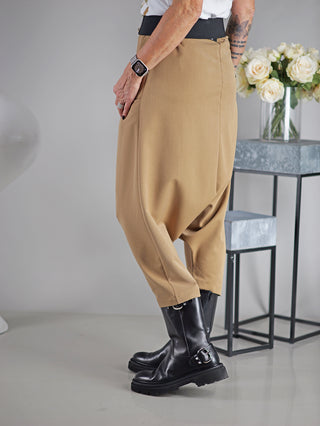 OFF#DLY Pant Susana camel, getragen von einer Person, zeigt eine lässige Haremshose mit weitem Schnitt und großer Einschubtasche, kombiniert mit schwarzen Stiefeln.