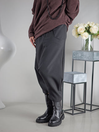 Person trägt OFF#DLY Pant Susana black, kombiniert mit schwarzem Stiefel und Halskette. Im Hintergrund eine Vase mit weißen Rosen auf einem Tisch.