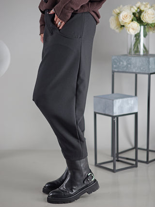 OFF#DLY Pant Susana black, getragen von einer Person. Schwarze Hose mit geradem Schnitt, kombiniert mit schwarzen Stiefeln. Im Hintergrund ein Tisch und weiße Rosen in einer Vase.