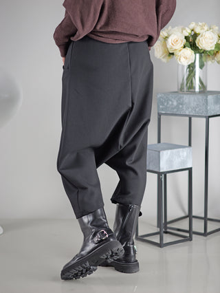 Person trägt OFF#DLY Pant Susana black, schwarze Hose kombiniert mit schwarzen Stiefeln. Im Hintergrund ein Tisch mit Vase und weißen Rosen, betont die Eleganz der Hose.