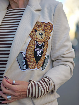 Person trägt den OFF#DLY Blazer Bear creme mit großem Bären-Patch auf der linken Seite; gerade Passform und angedeutete Taschen. Blazer mit einem Knopf, empfohlen für Größen 34 bis 40.