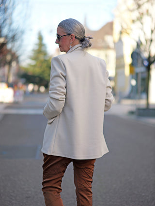 Eine Frau trägt den OFF#DLY Blazer Bear creme mit großem Bären-Patch und angedeuteten Taschen, präsentiert in einer urbanen Umgebung.
