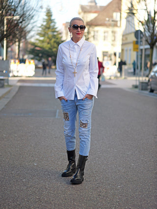 Frau trägt OFF#DLY Slimfit Bluse Tina white mit Knopfleiste, kombiniert mit blauen Jeans und schwarzen Stiefeln. Bluse ist schmal geschnitten und passt eng anliegend.