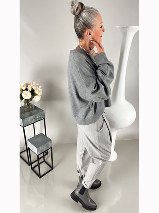 OFF#DLY Stripes Pant Lola grey, eine lässige Bundfaltenhose mit tiefem Schritt, seitlichen Einschubtaschen und Gummibund hinten, getragen von einer Person neben einer Skulptur.
