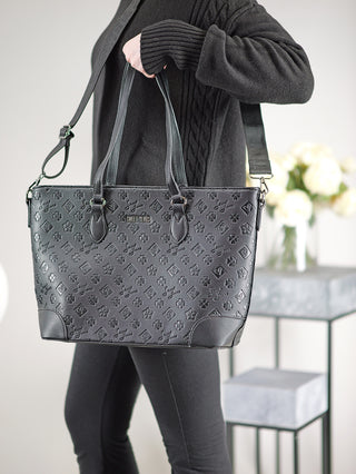 Person hält Sweet Years Shopper schwarz mit geprägtem Design, verstellbarem Trageriemen und mehreren Reißverschlussfächern. Großes Format, ideal als modischer und funktionaler Begleiter.