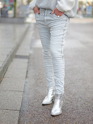 Person trägt OFF#DLY Pant Tina grey, eine leichte Joggpant mit seitlicher Kettenkordel und Gummibund, kombiniert mit silbernen Stiefeln.